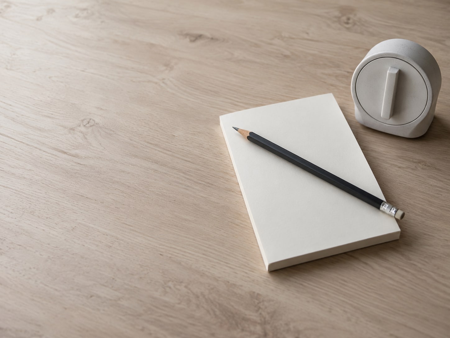 A pencil resting across a blank checklist pad on a clean desk, with a small kitchen timer beside it.