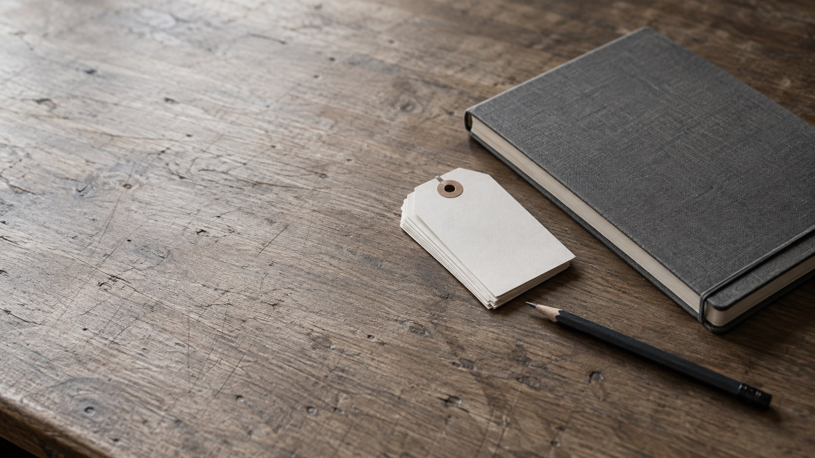Una pequeña pila de etiquetas de papel en blanco y un cuaderno cerrado junto a un lápiz sobre un escritorio de madera liso.