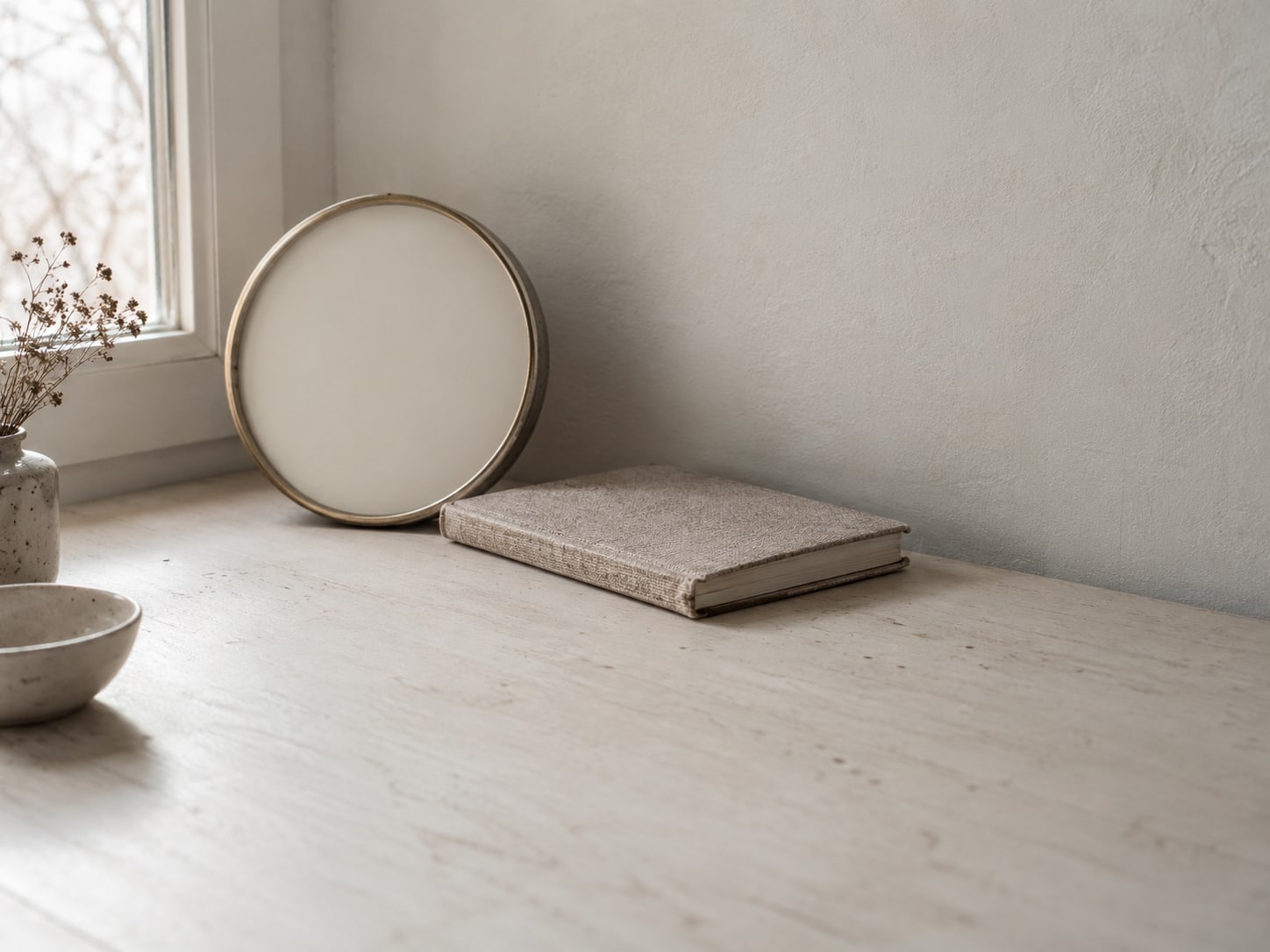 Un reloj de pared con la carátula en blanco junto a una agenda de citas cerrada sobre un escritorio claro.