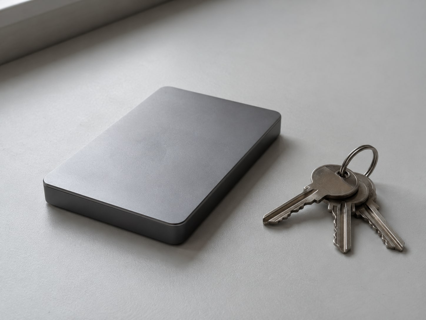 A small external hard drive sitting beside a ring of plain keys on a clean desk surface.