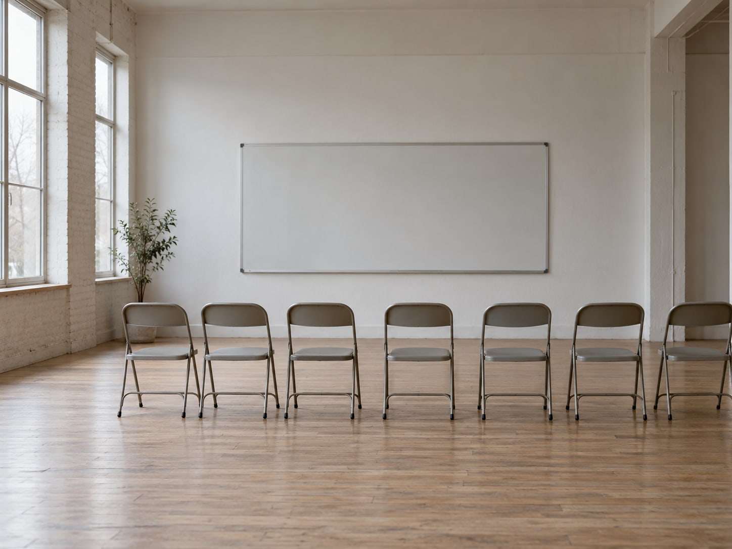 A row of empty folding chairs facing a blank whiteboard in a bright community room.