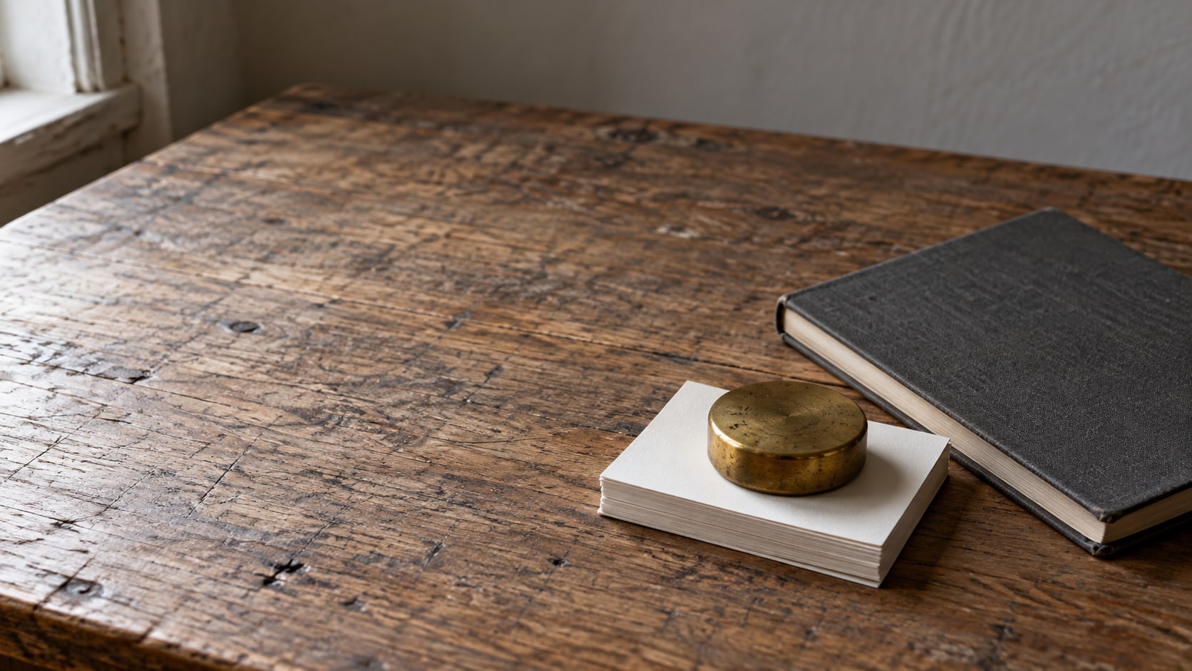 A brass paperweight resting on a small stack of blank index cards beside a closed notebook on a wooden desk.