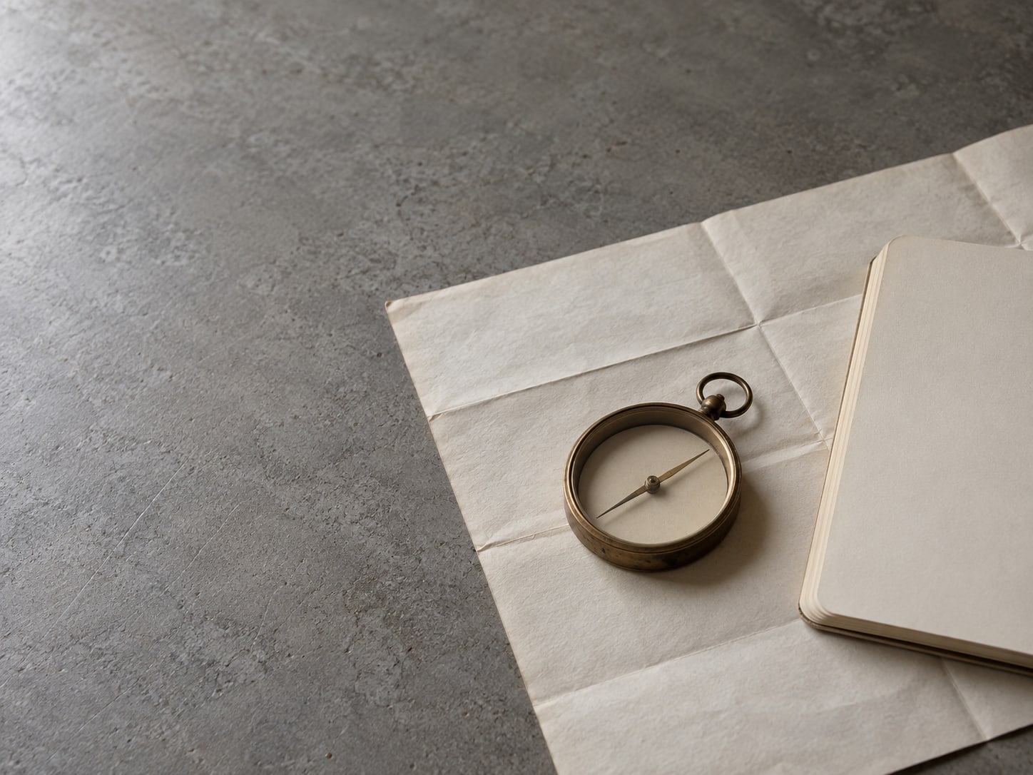 A small brass compass lying on a folded paper map beside a blank notepad.