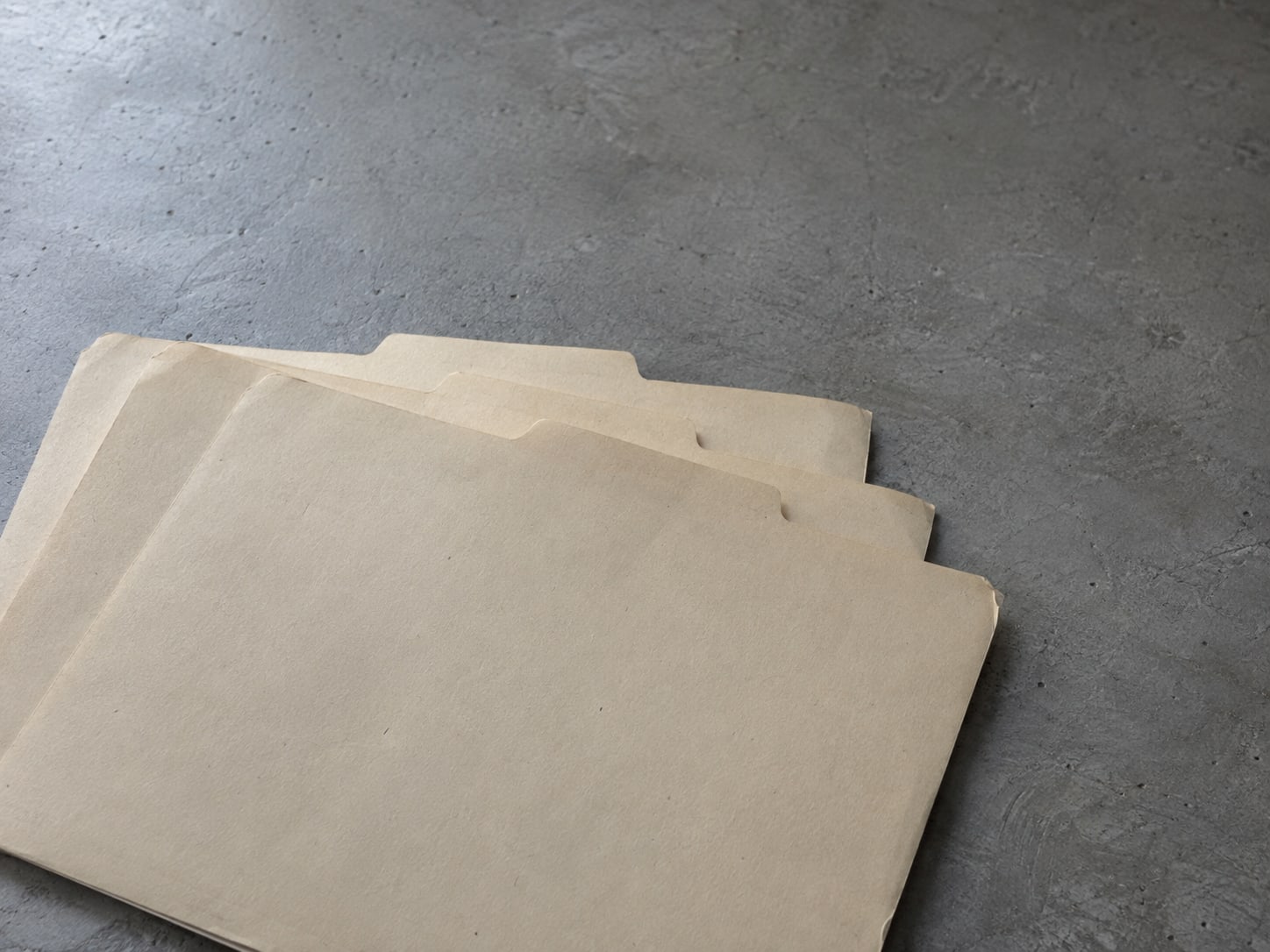 Three empty manila folders fanned out on a gray desk beside a closed notebook.