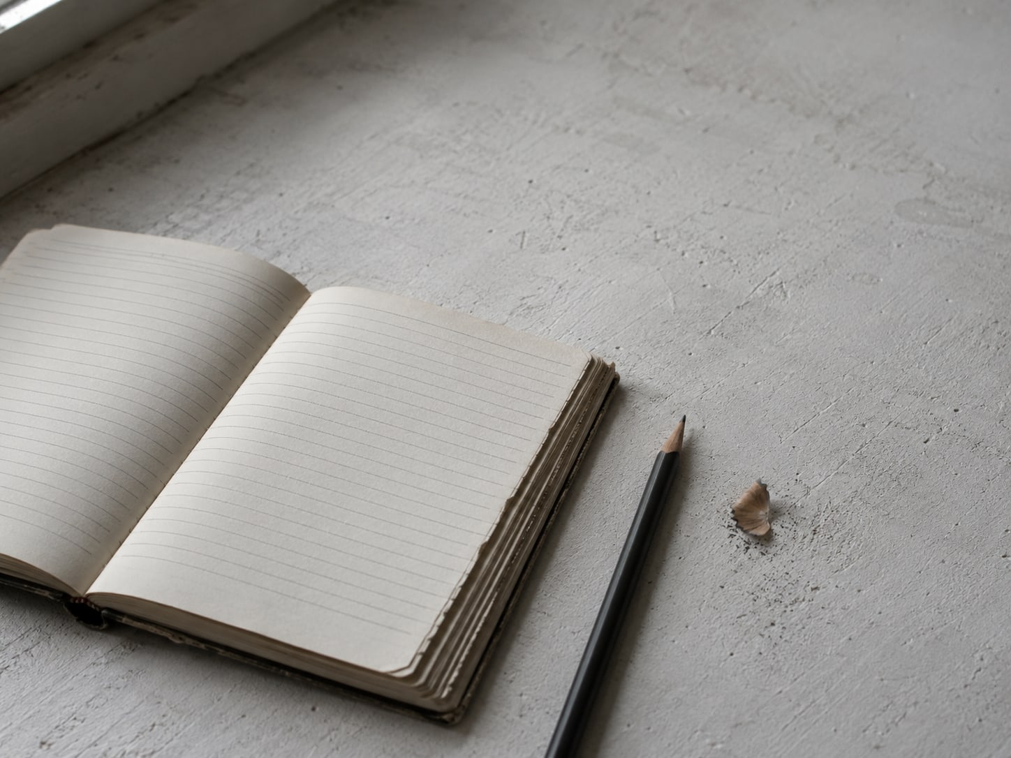 A paper ledger with blank ruled lines beside a sharpened pencil on a plain surface.