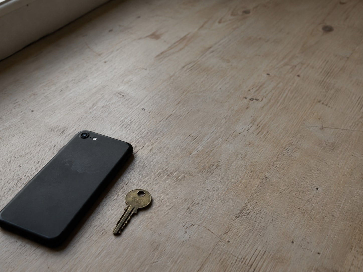 A single brass key on a plain wooden desk beside a switched-off phone lying face down.