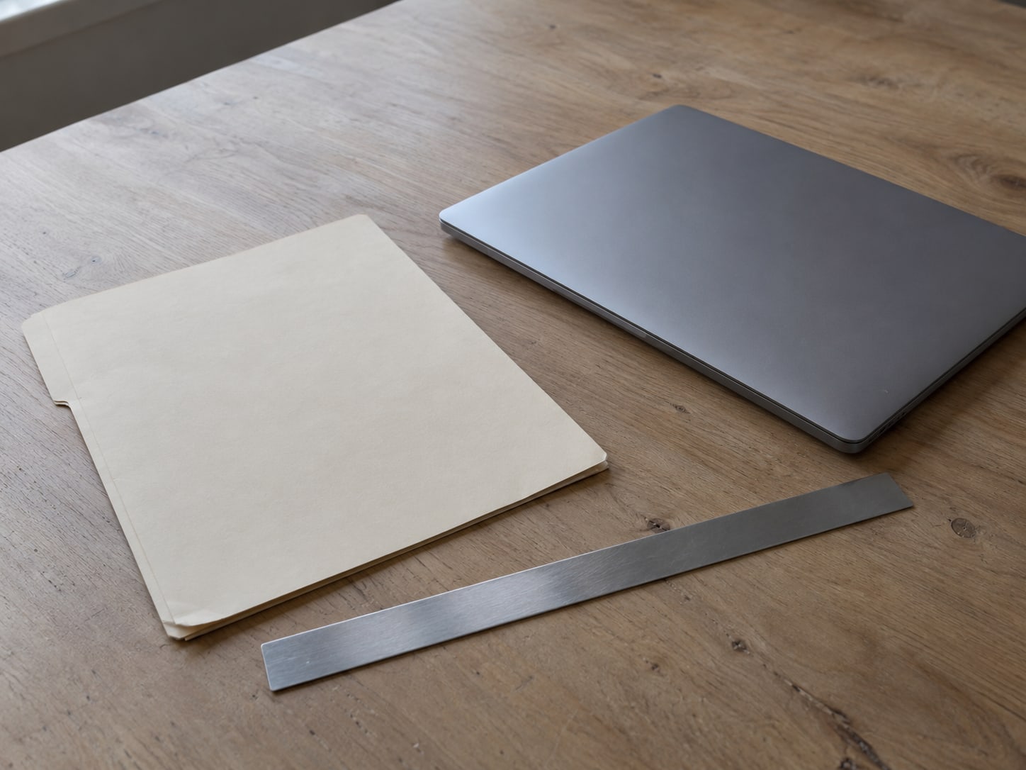 A paper folder and a ruler resting on a clean desk beside a closed laptop.