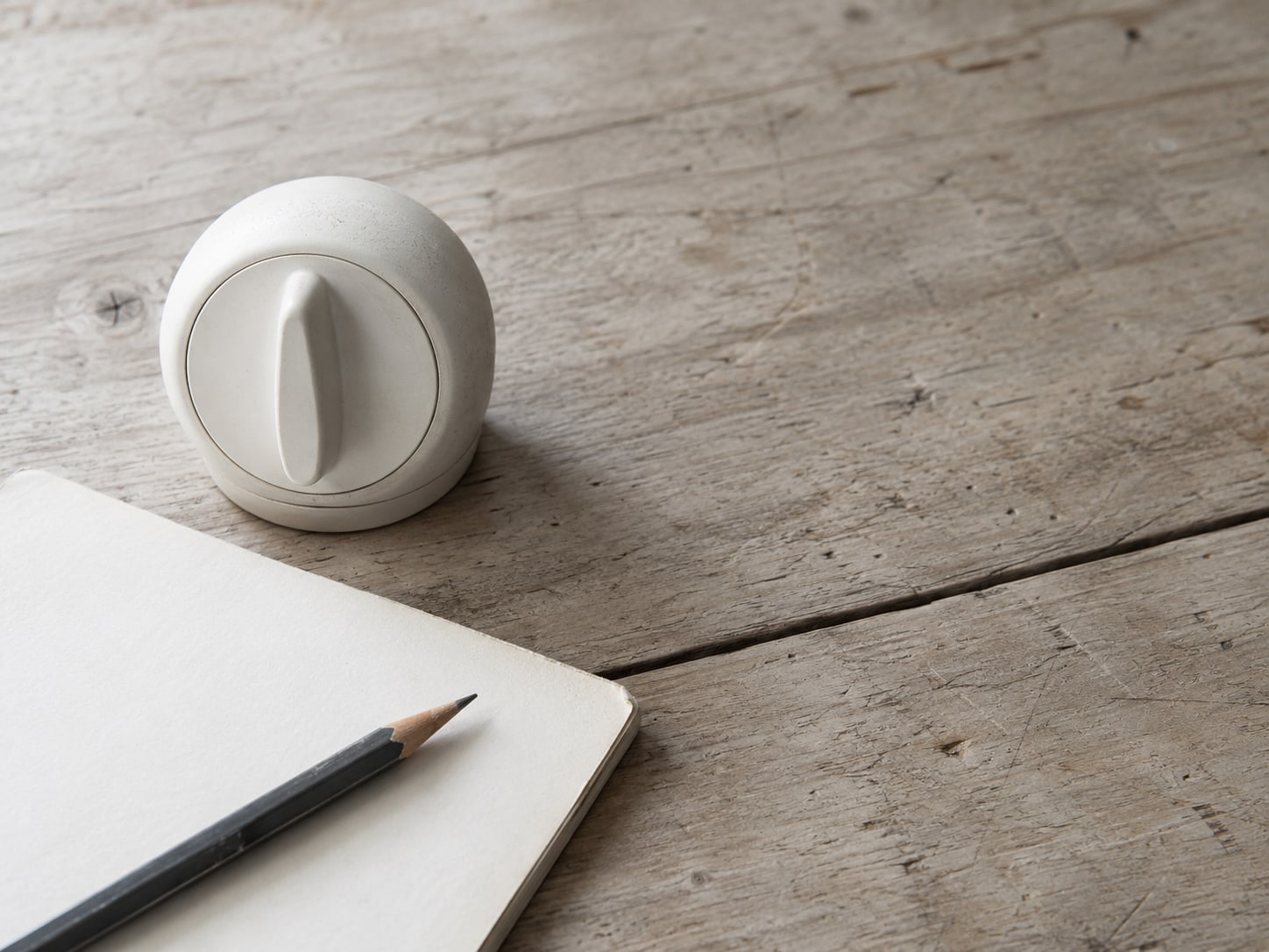 A white kitchen timer beside a pencil and a blank notepad on a wooden table.