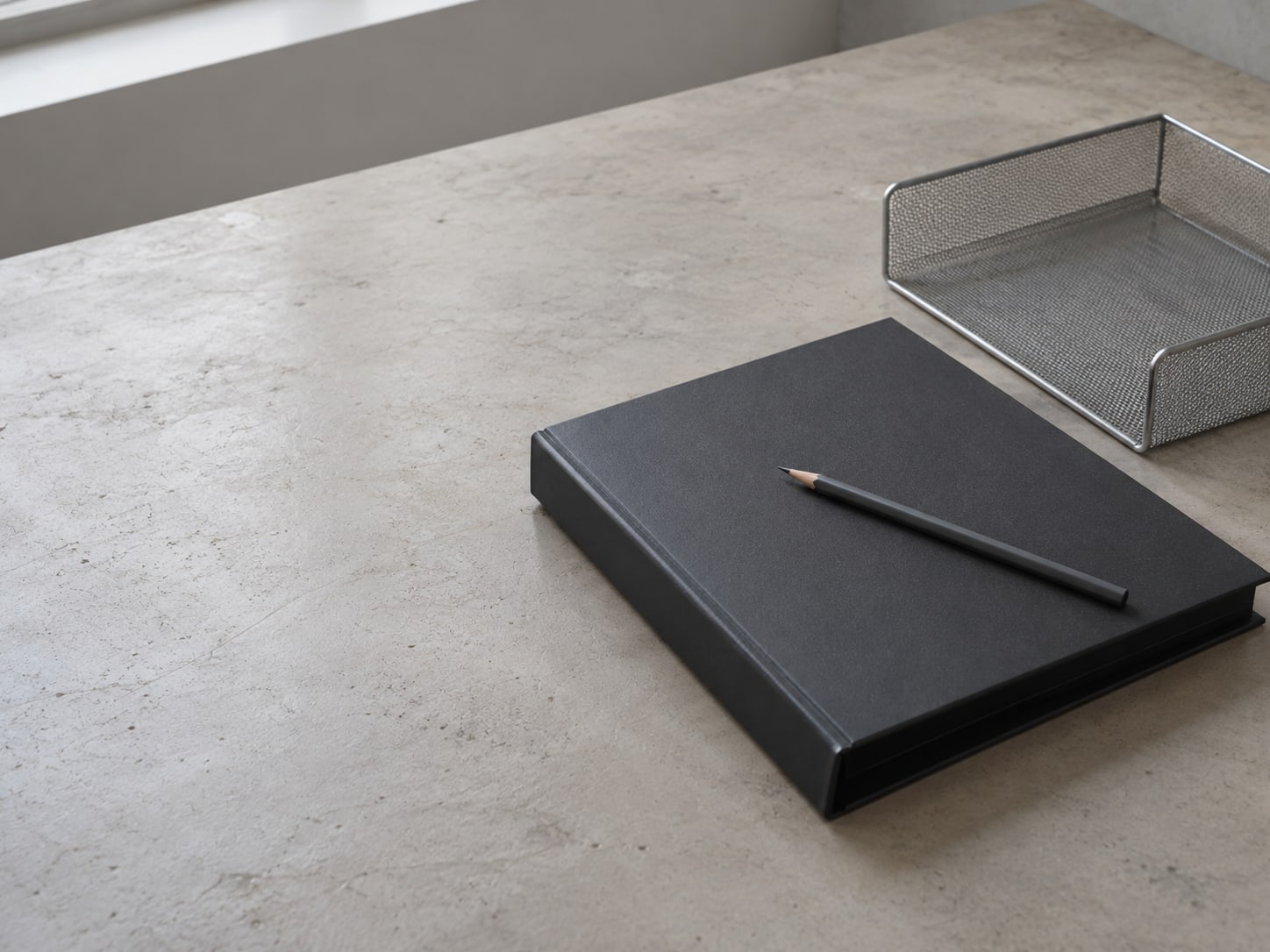 A closed binder with a pencil resting across its cover on a clean desk, next to an empty tray.