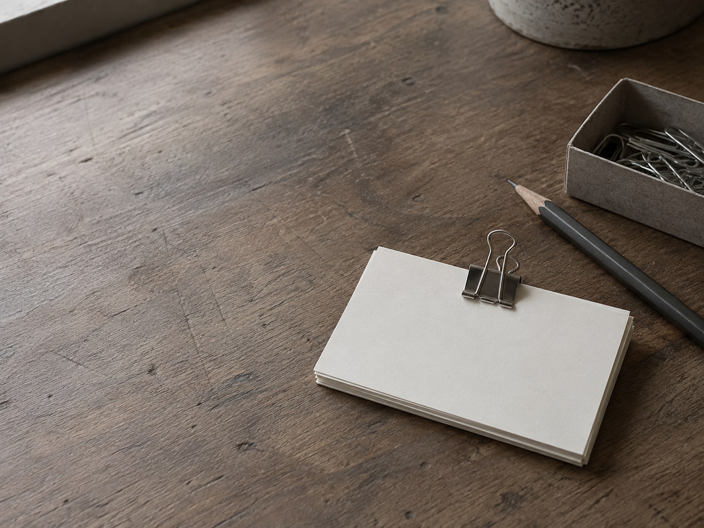 Several blank index cards clipped together on a desk next to a pencil and a small box of paper clips.