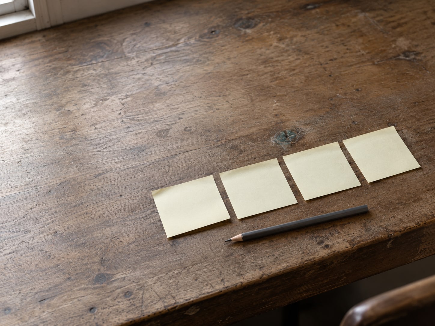 A row of blank sticky notes on the edge of a desk beside a pencil.