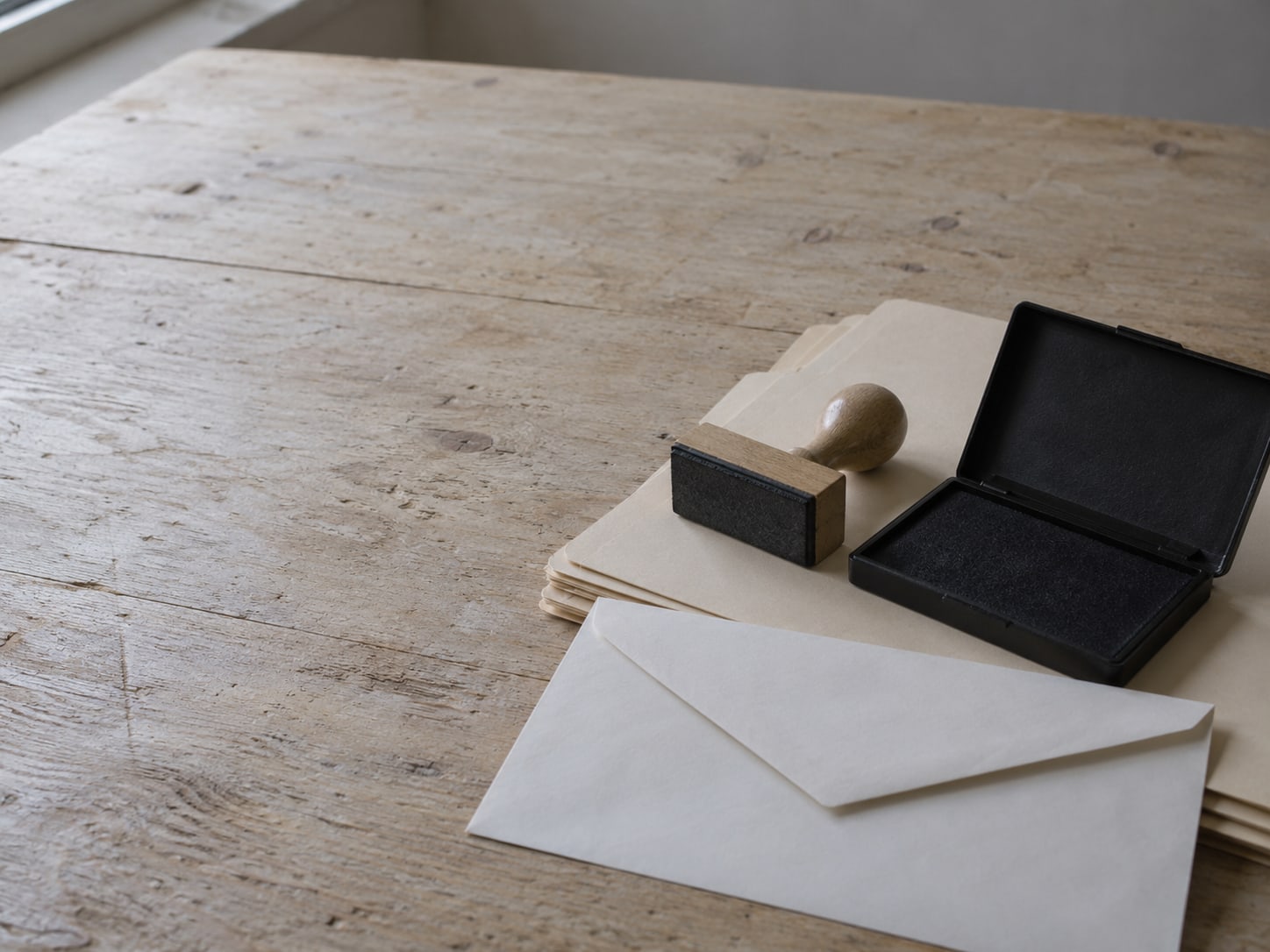 A rubber stamp and an empty ink pad sitting on a stack of plain folders next to a blank envelope.
