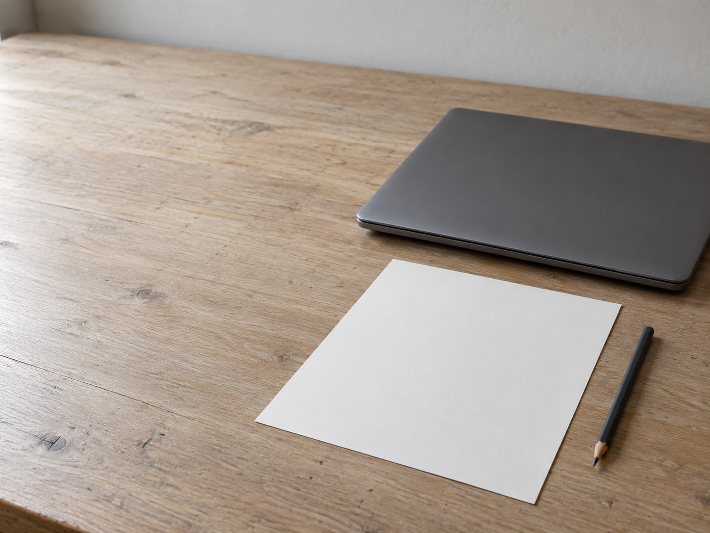 Una laptop cerrada junto a un lápiz y una lista de verificación en papel en blanco sobre un escritorio de madera.