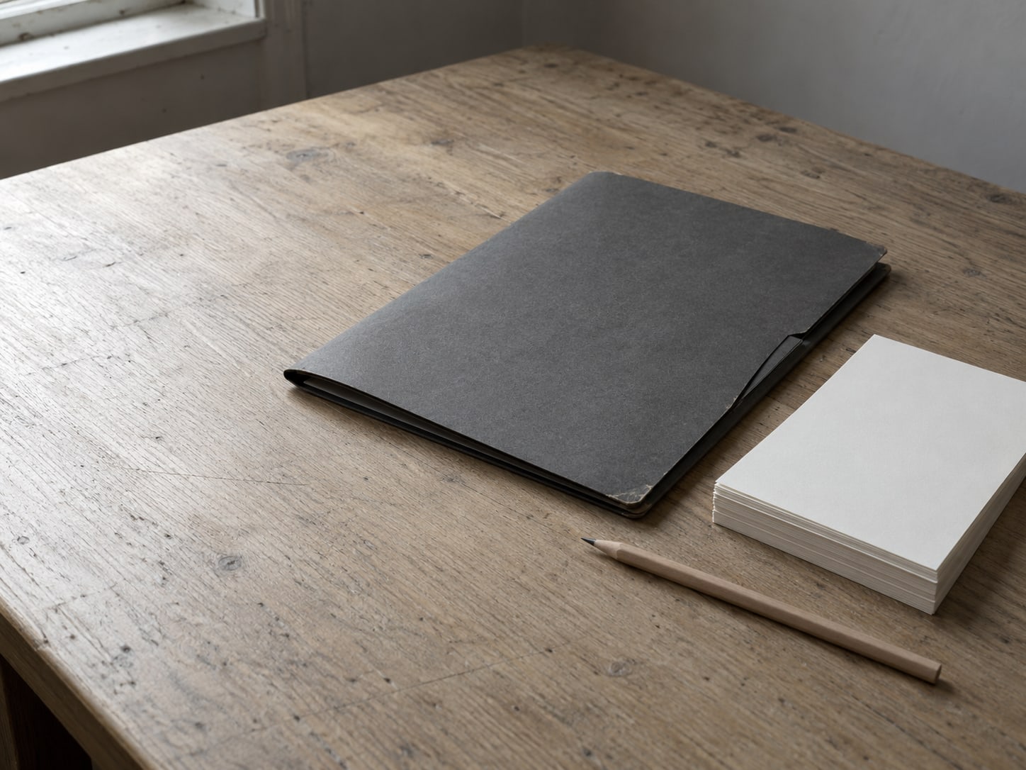 A closed folder beside a pencil and a small stack of blank invoice pads on a desk.