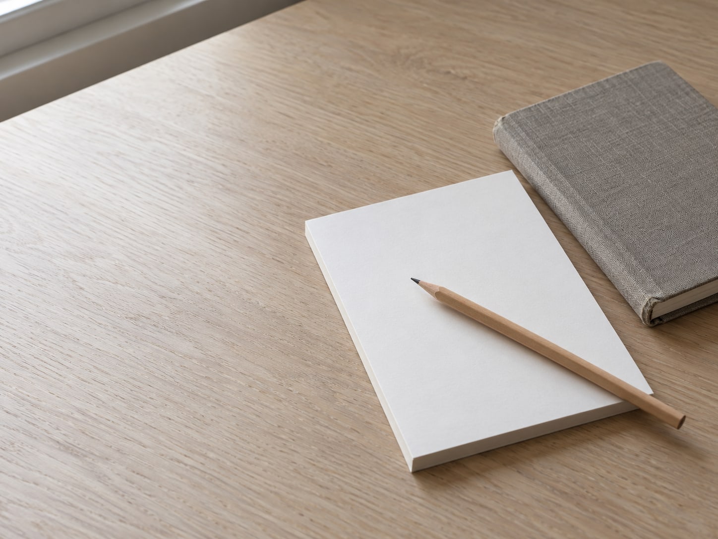 A pencil lying across a blank checklist pad next to a small closed notebook on a clean desk.