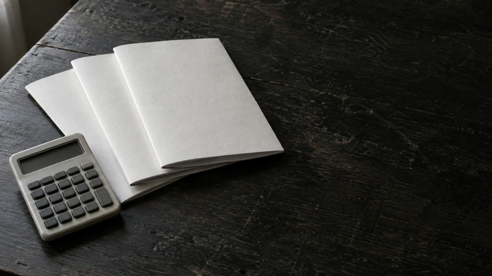 Three blank folded proposals and a small calculator switched off, arranged on a dark wooden desk.