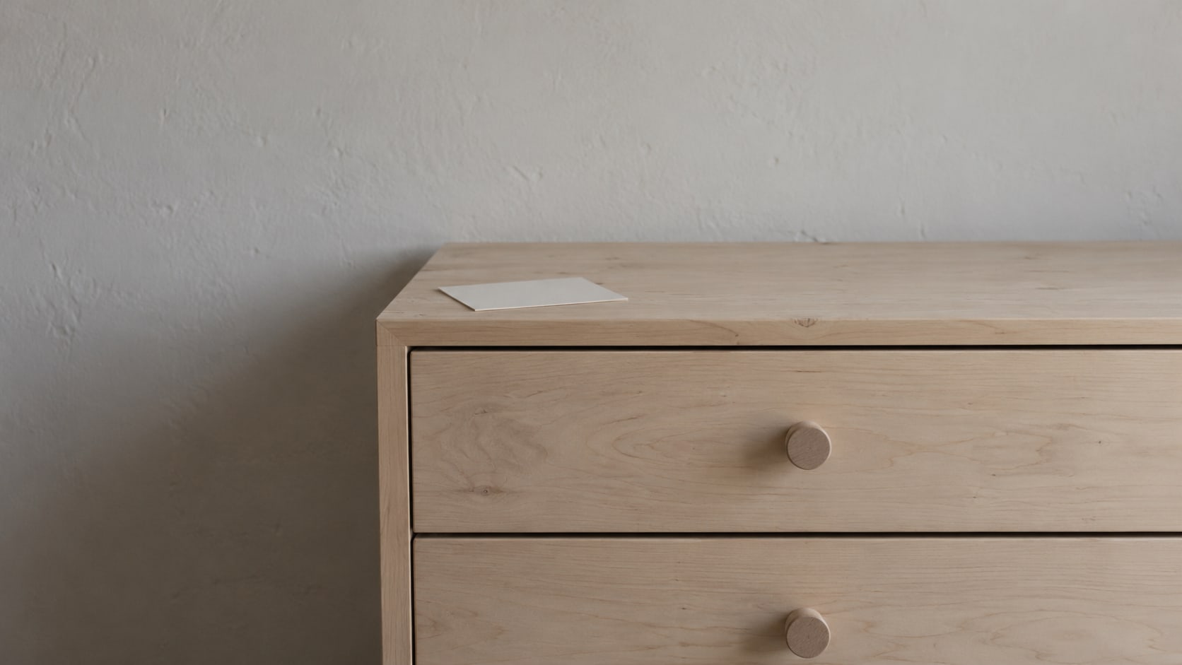 A row of plain wooden drawer pulls on a closed cabinet, with a single blank index card resting on top.