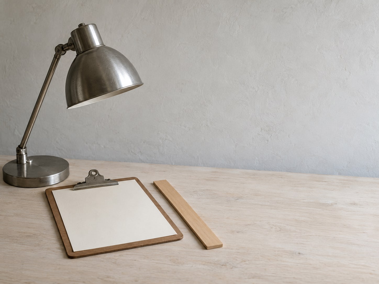 A single desk lamp, a ruler and a plain clipboard with blank paper on a clean surface.
