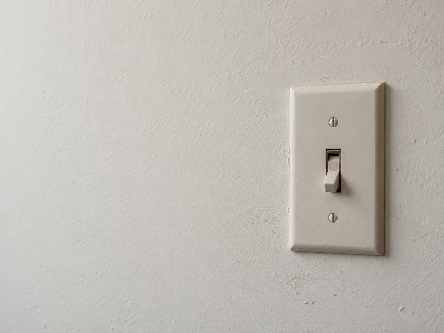 A single plain wall light switch in the off position on a bare painted wall.