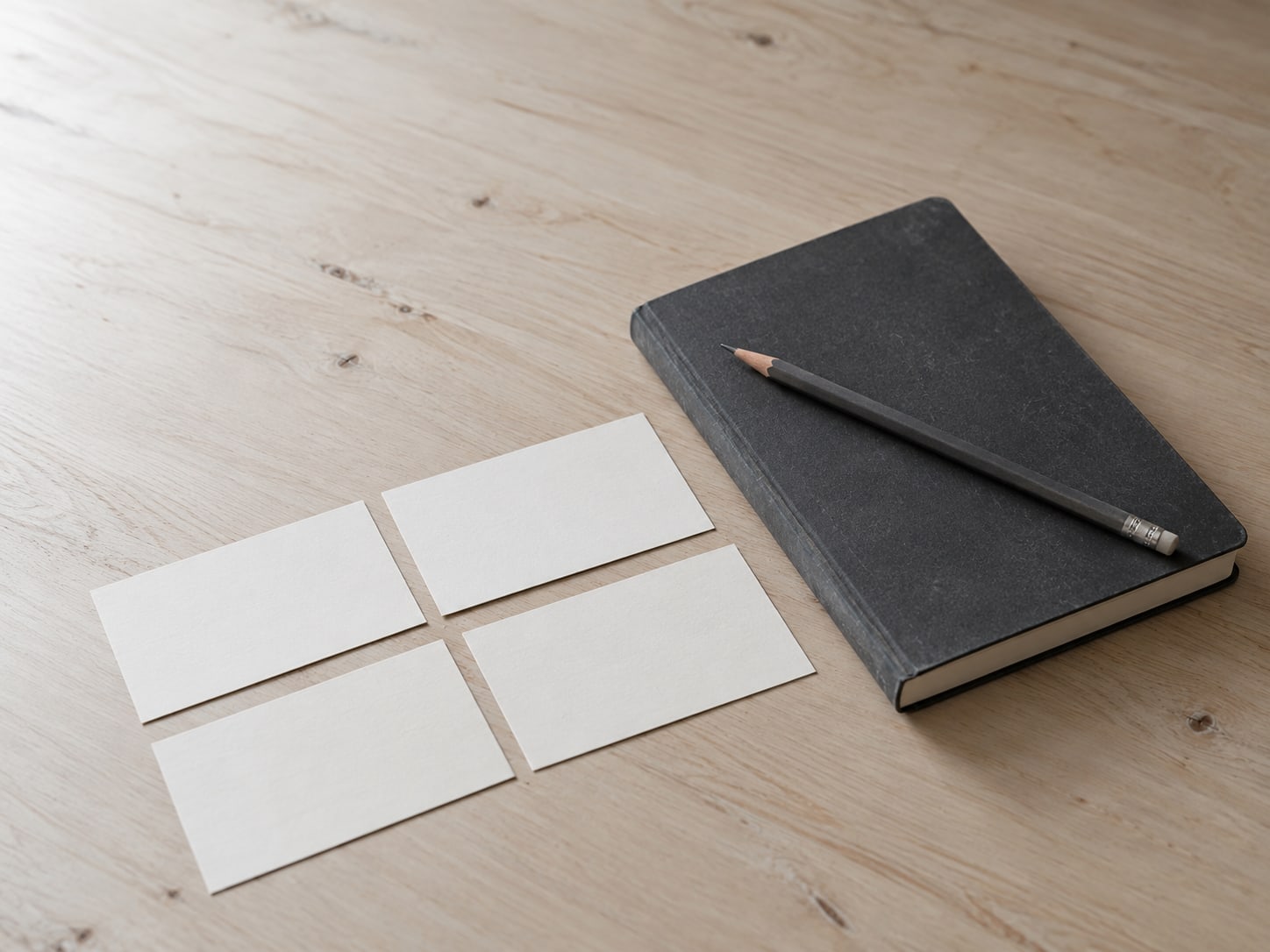 A closed notebook with a pencil on top, beside a few blank index cards on a clean desk.