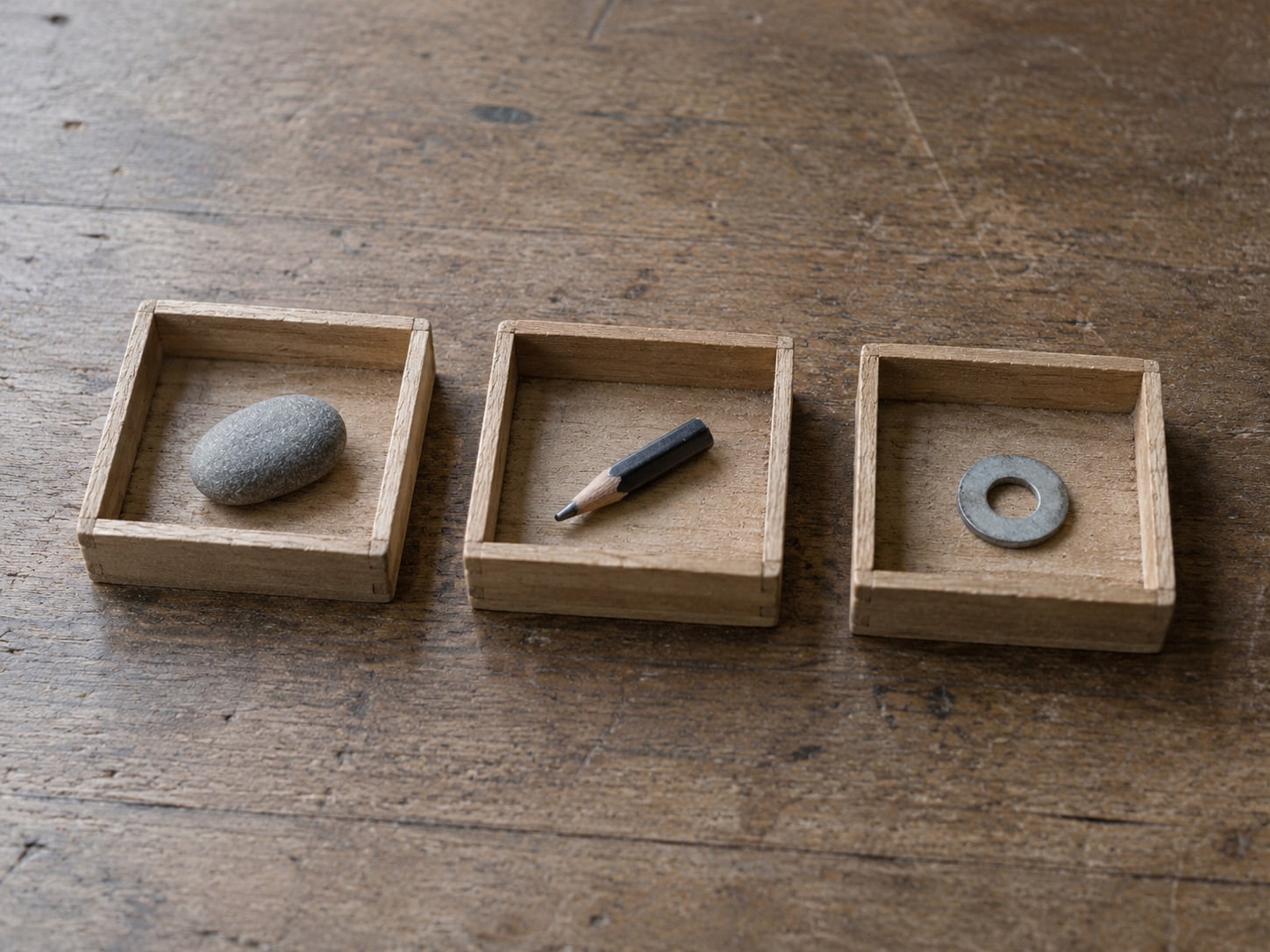 A row of three wooden trays on a plain desk, each holding a different small object.