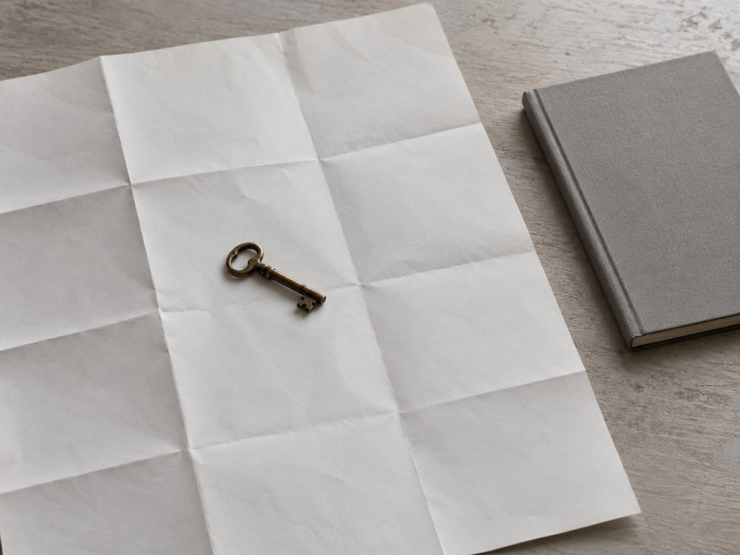 A small brass key resting on a folded paper map of a town, next to a closed notebook.