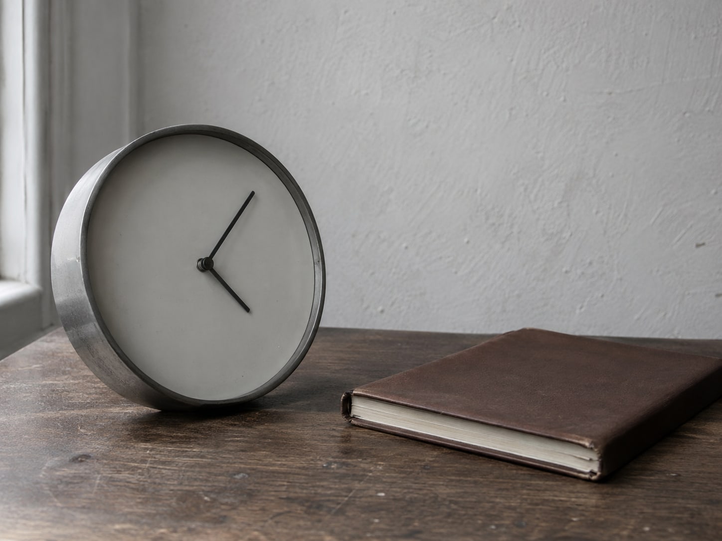 A wall clock stopped at an unreadable angle beside a closed wooden appointment book.