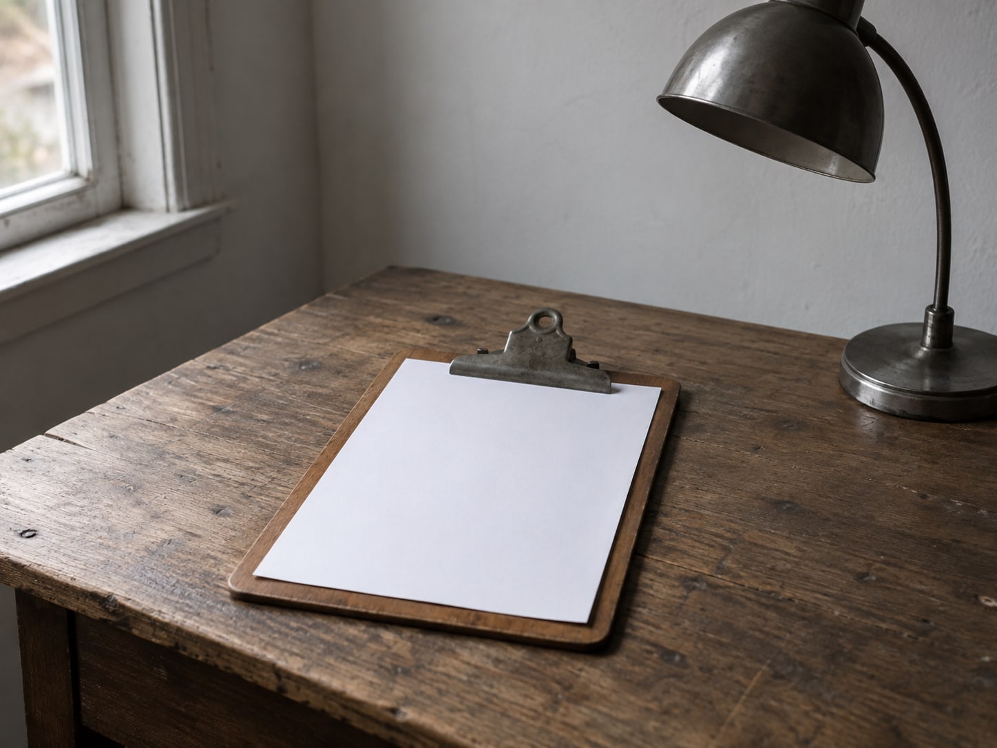 A wooden clipboard holding a blank checklist sheet beside an unplugged desk lamp.