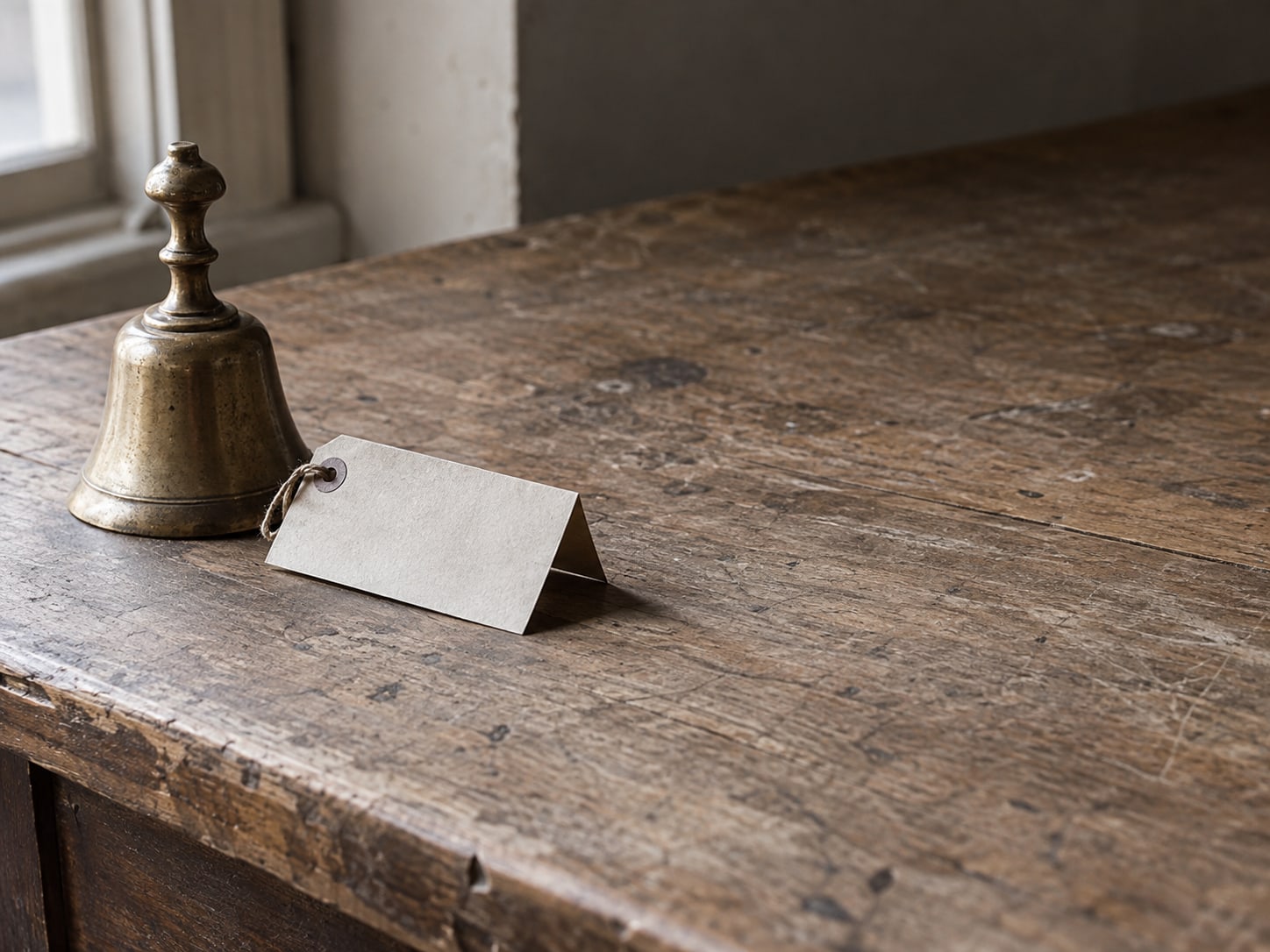 A small brass bell and a folded blank paper price tag on a bare shop counter.