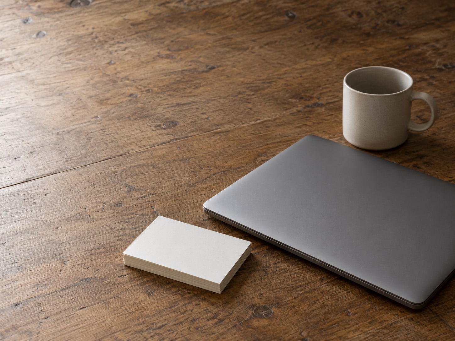 A closed laptop beside a stack of blank index cards and a ceramic mug on a tidy desk.