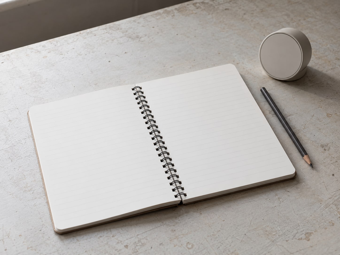 Una libreta de espiral abierta con hojas rayadas en blanco, junto a un lápiz y un temporizador de cocina pequeño.