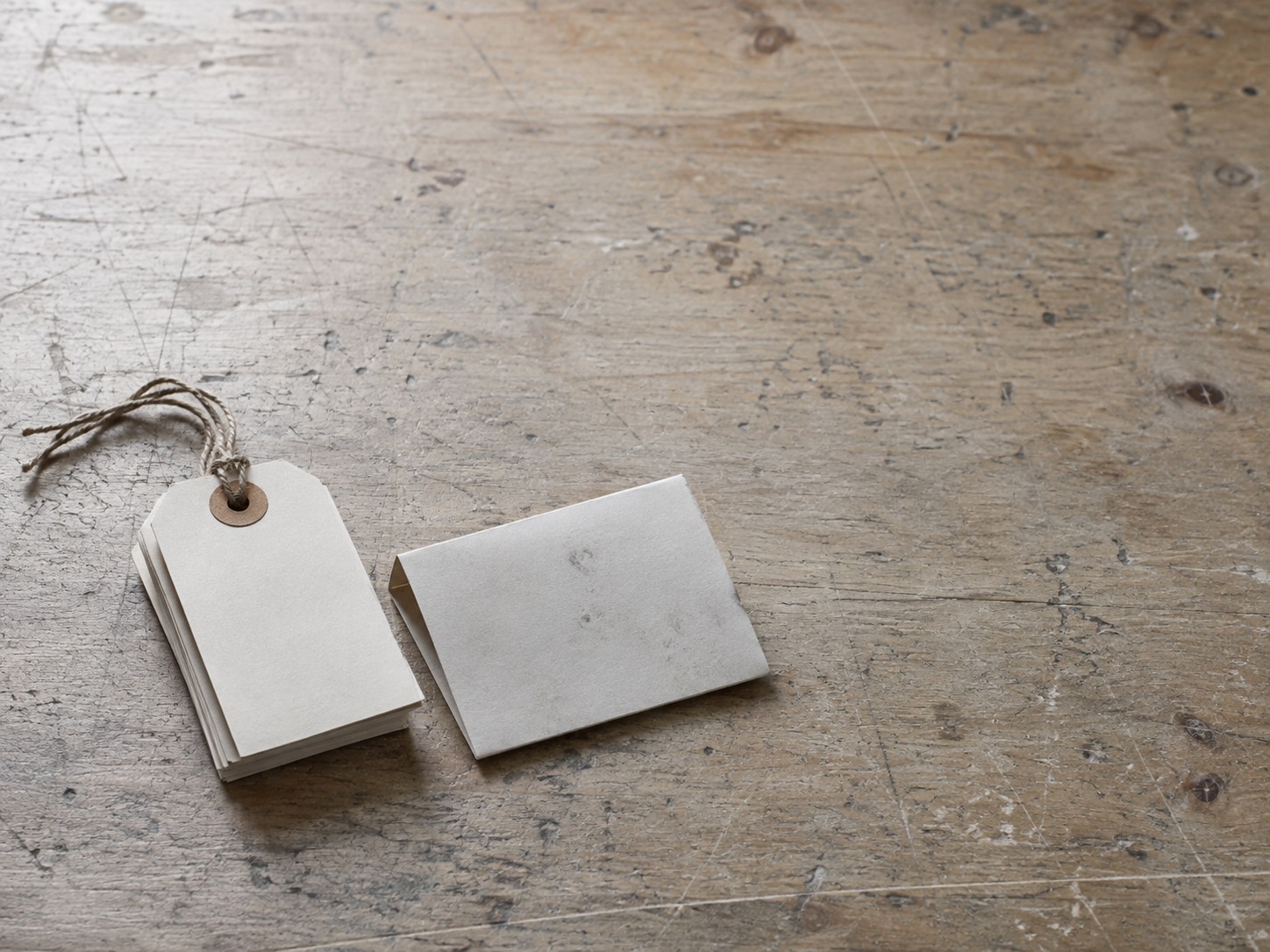 Una pequeña pila de etiquetas de precio en blanco de papel atadas con un cordón junto a una etiqueta de envío doblada con marcas de lápiz tenues sobre una mesa de trabajo.