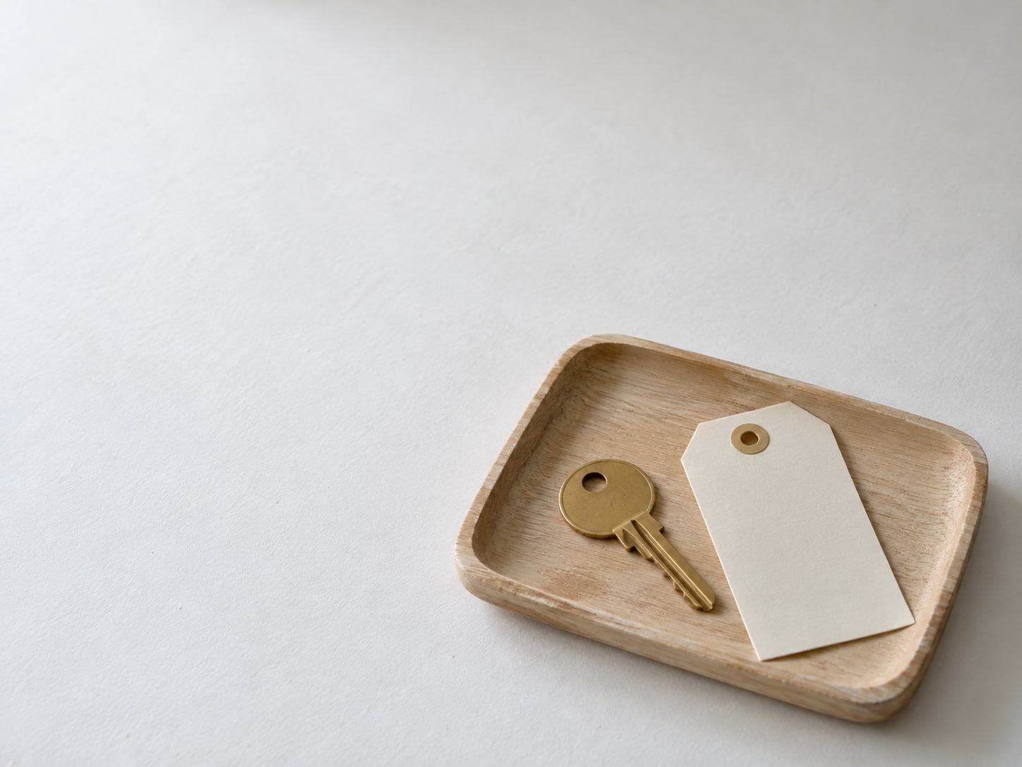 A plain brass key on a small wooden tray next to a blank cardstock tag with no writing.