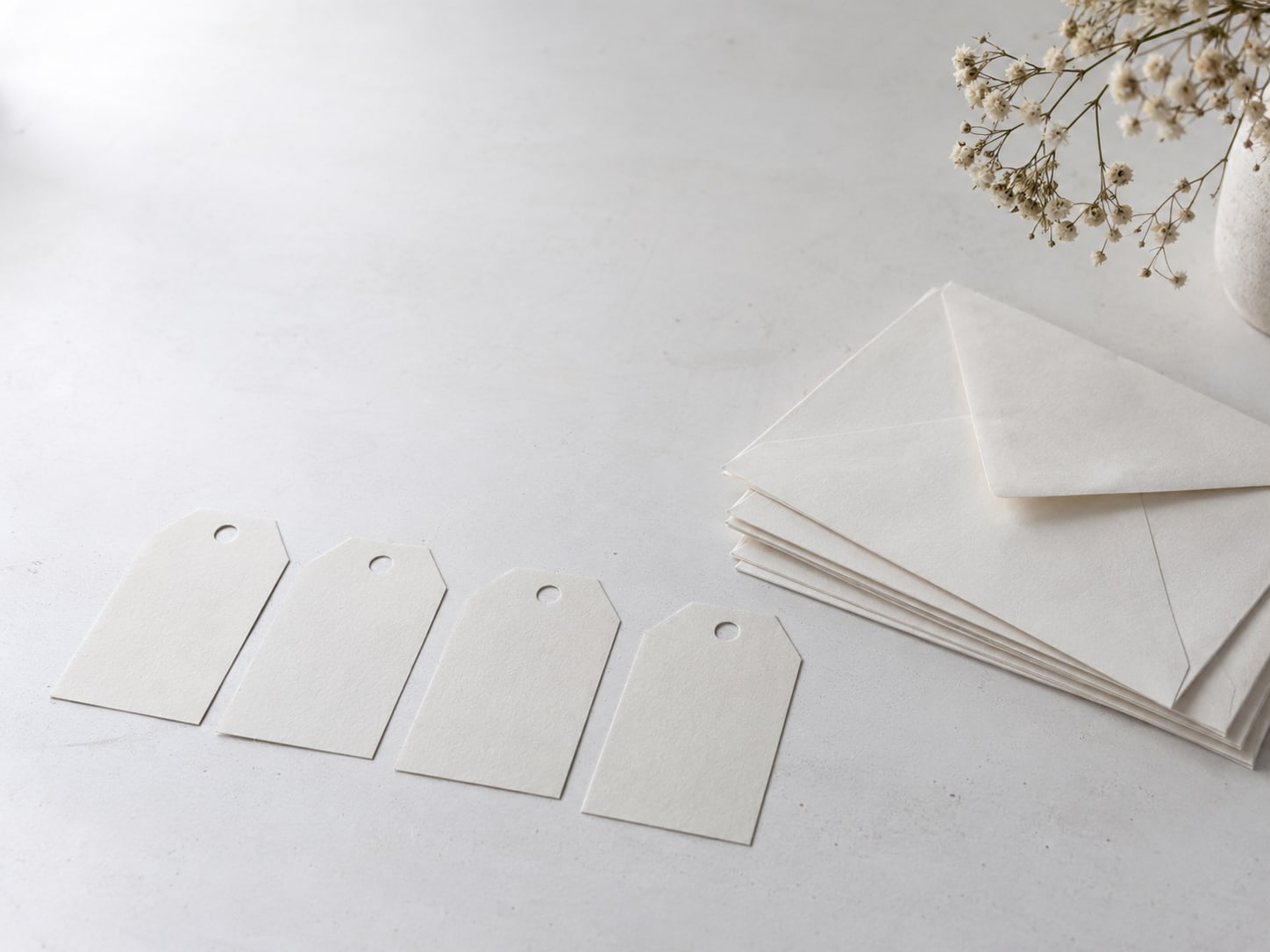 A tidy row of blank paper labels on a white table beside a small stack of unmarked envelopes.