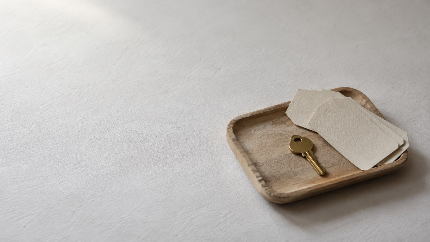 A plain brass key on a small wooden tray beside blank cardstock tags on a white table.