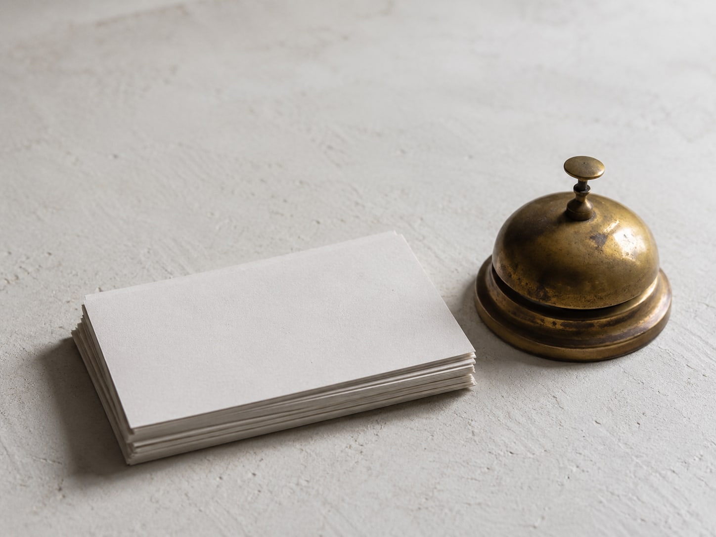 A tidy stack of blank appointment cards beside a small brass desk bell on a pale surface.
