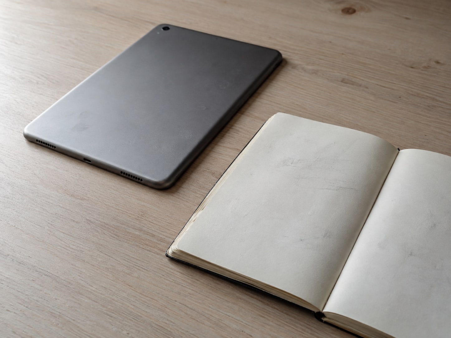 A switched-off tablet lying face down next to a plain notebook with faint, unreadable pencil marks.