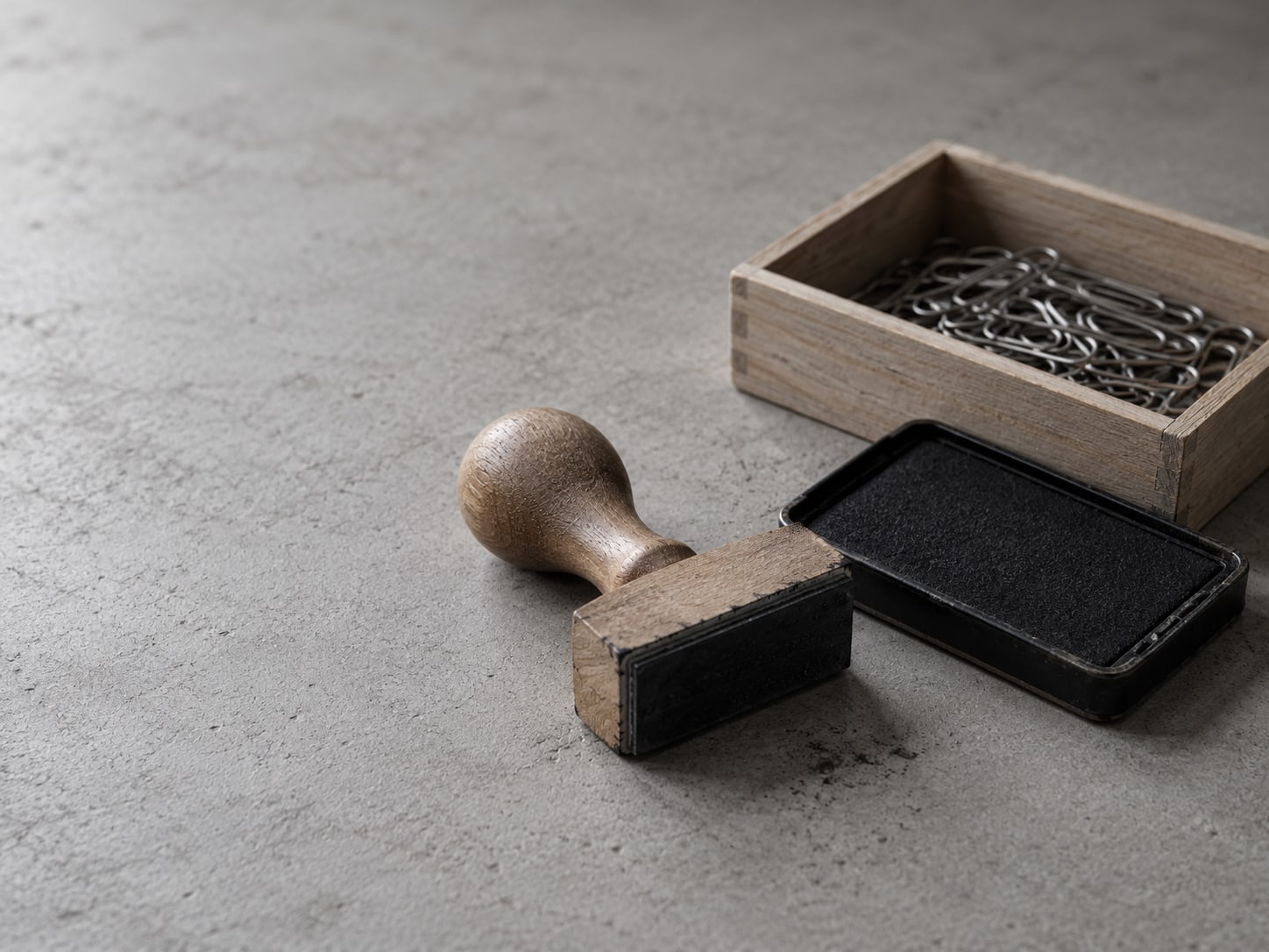 A rubber stamp and a blank ink pad next to a small wooden tray of paper clips.