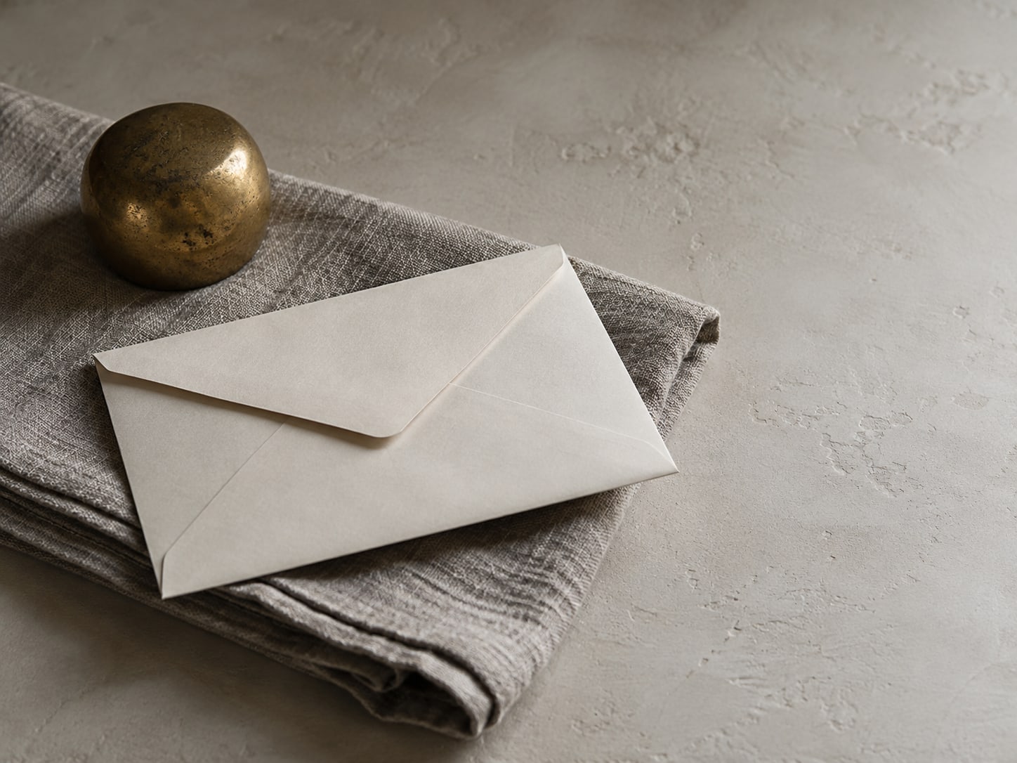 A single blank envelope resting on a folded gray cloth next to a small brass paperweight.