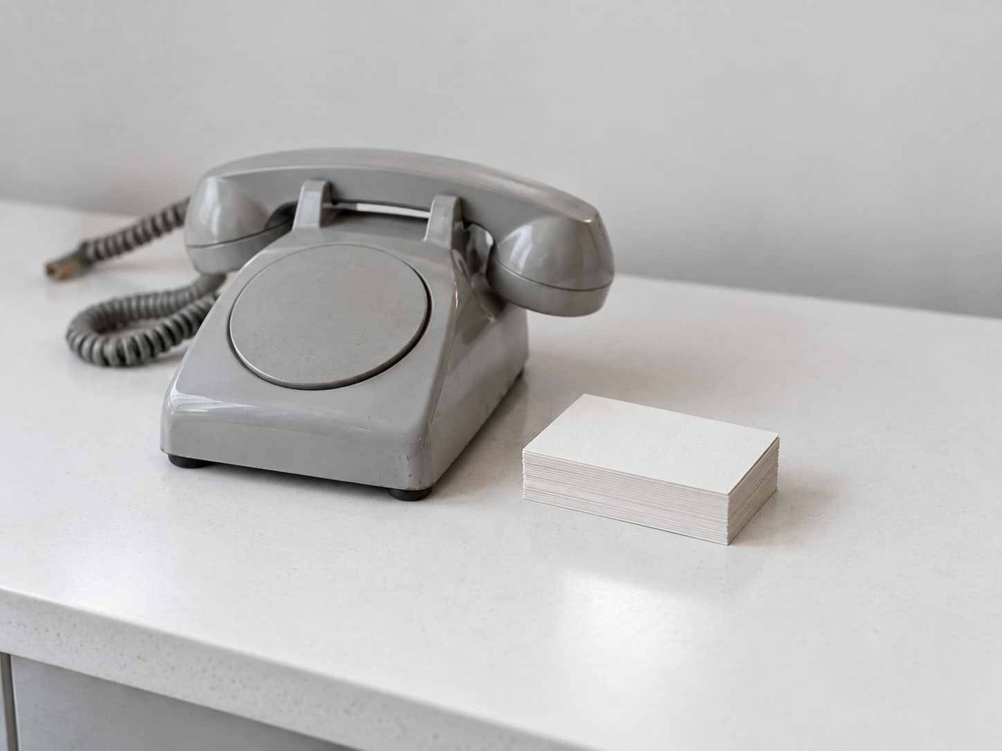 An unplugged desk telephone beside a stack of blank business cards on a white shop counter.