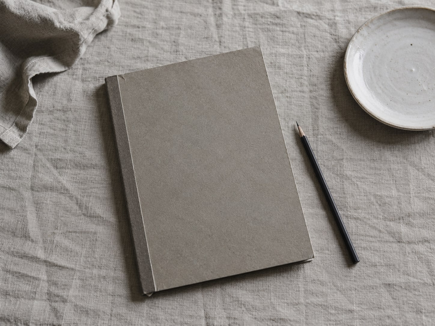 A flat lay of a closed menu folder, a pencil and a small plate on a plain linen cloth