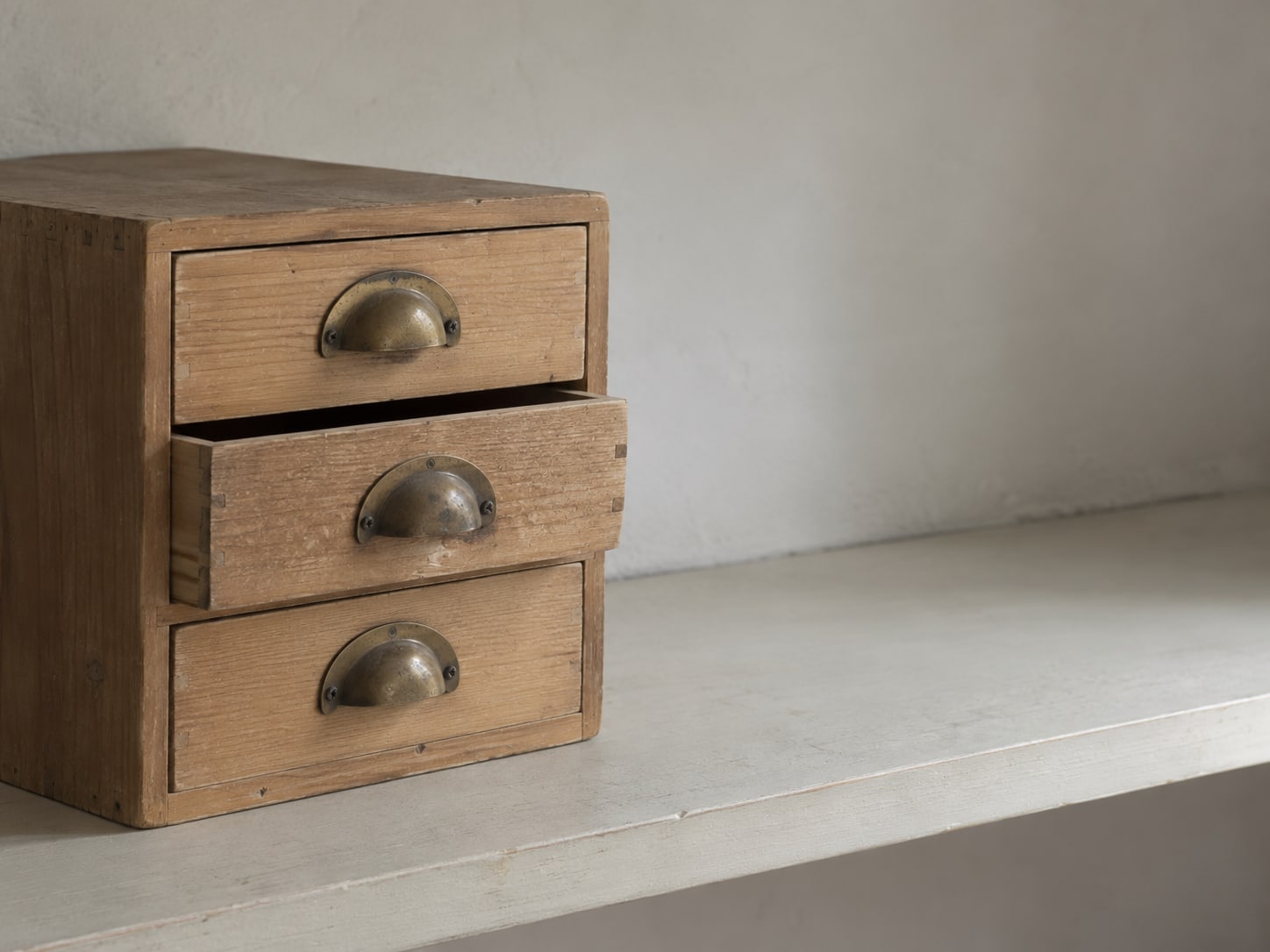 A tidy row of three small wooden drawers with brass pulls, one slightly open, on a plain shelf.
