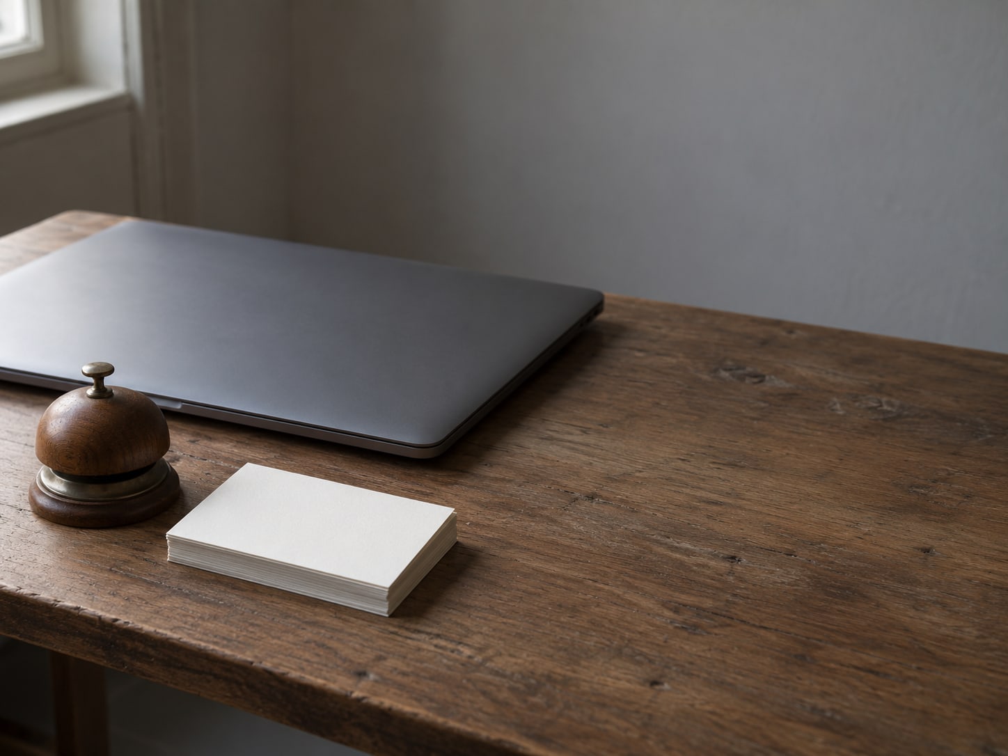 A wooden desk bell and a small stack of blank index cards beside a closed laptop.
