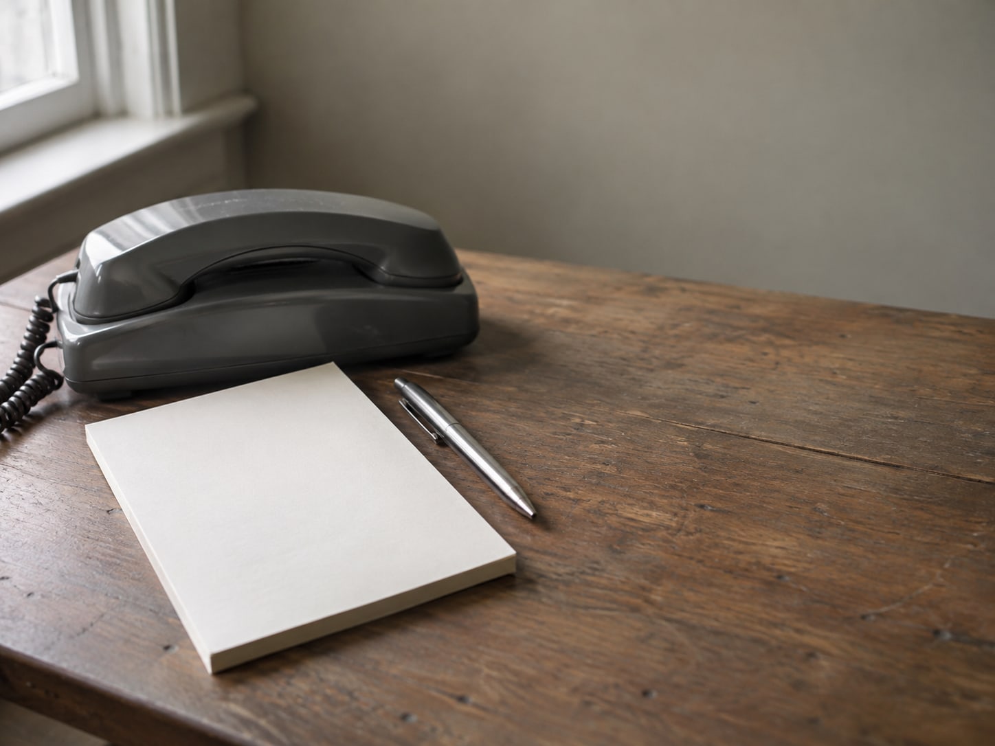 A desk telephone handset resting in its cradle beside a blank notepad and a pen.