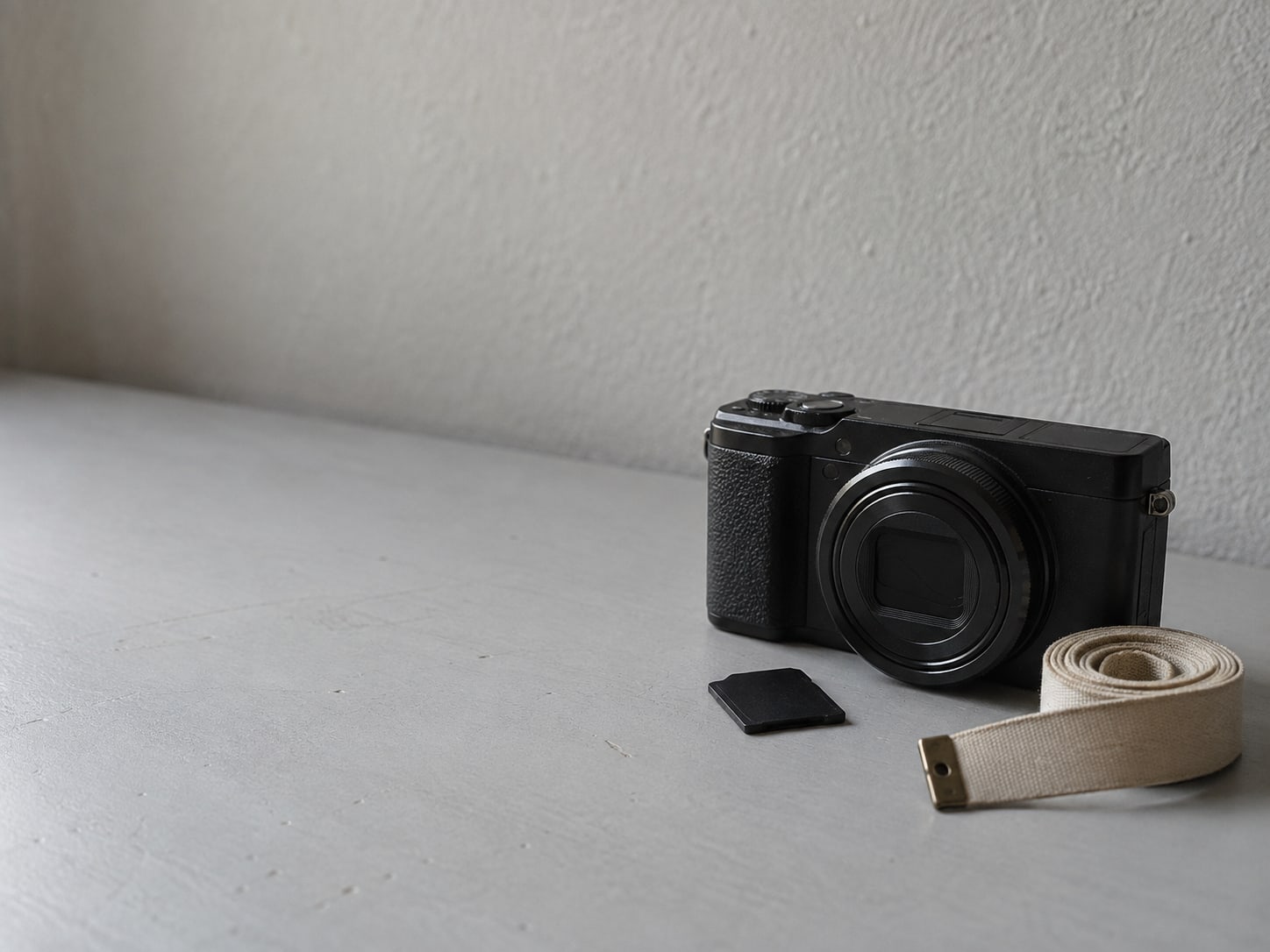 A small digital camera with its memory card lying beside it on a light gray desk, next to a folded measuring tape.
