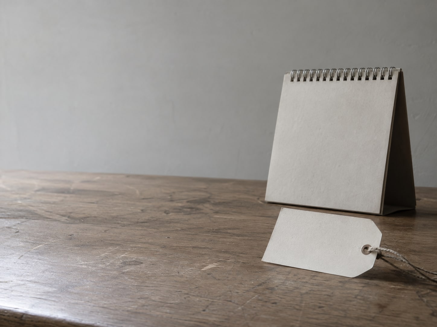 Una etiqueta de papel en blanco atada con cordel descansando junto a un calendario de escritorio cerrado sobre un mostrador de madera.