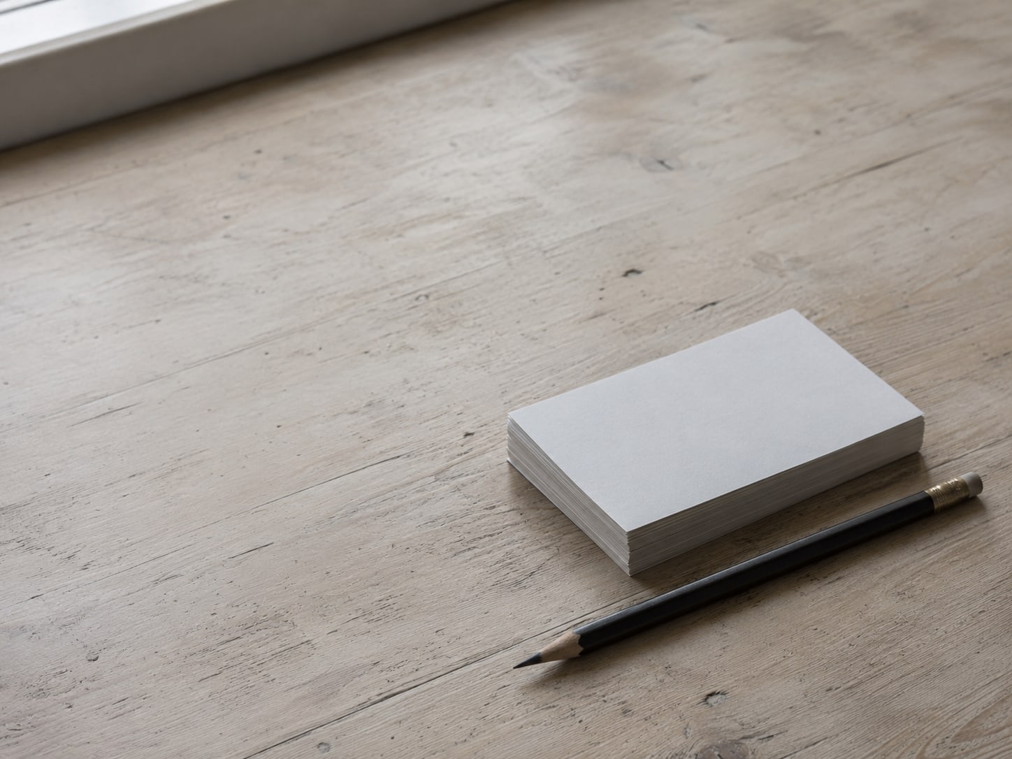A small stack of blank index cards beside a sharpened pencil on a pale wooden desk.