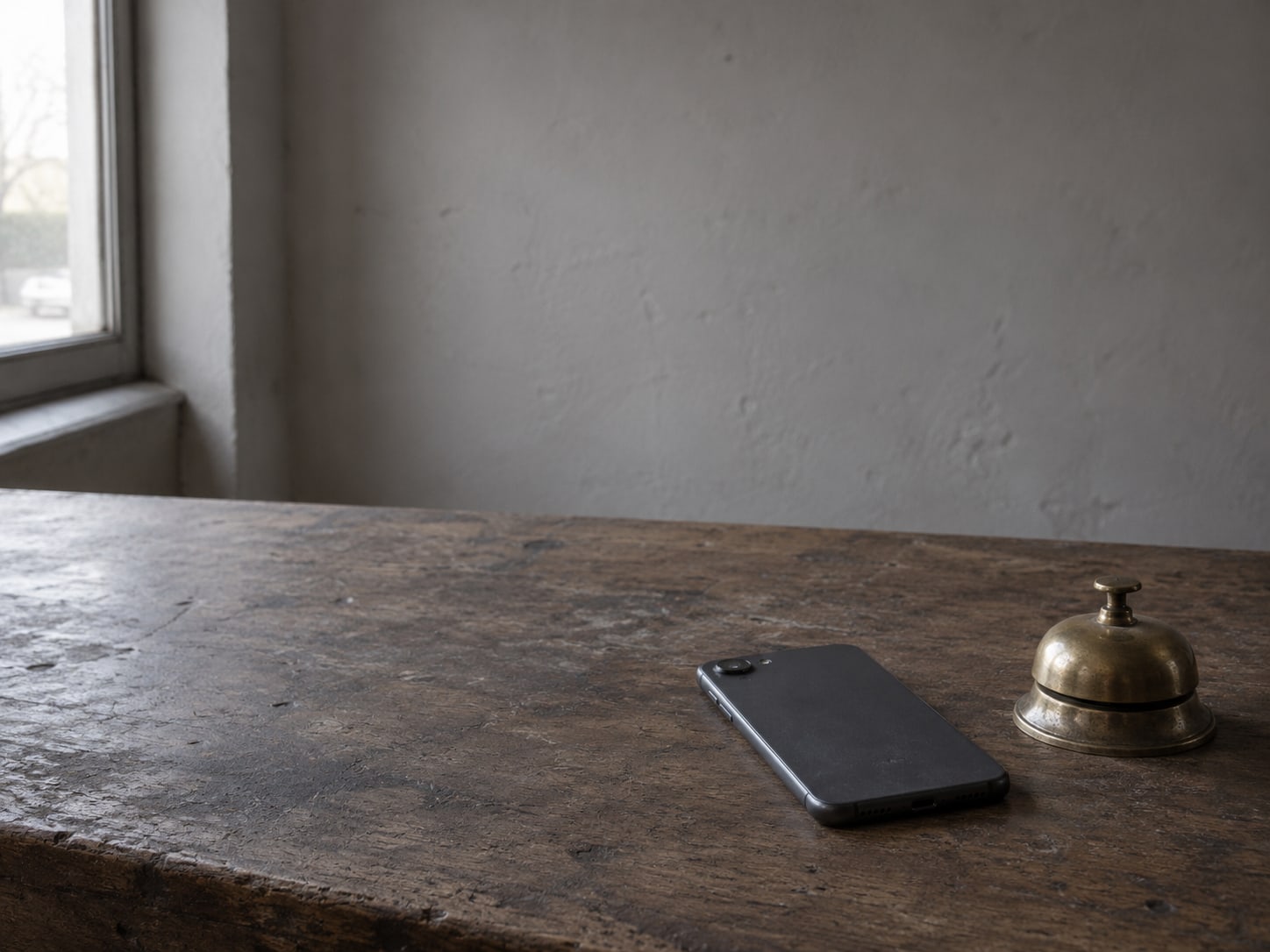 A smartphone lying face down on a worn shop counter beside a small brass bell.