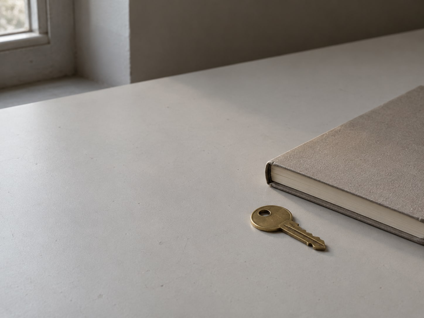A single brass key lying beside a closed notebook on a clean desk surface.