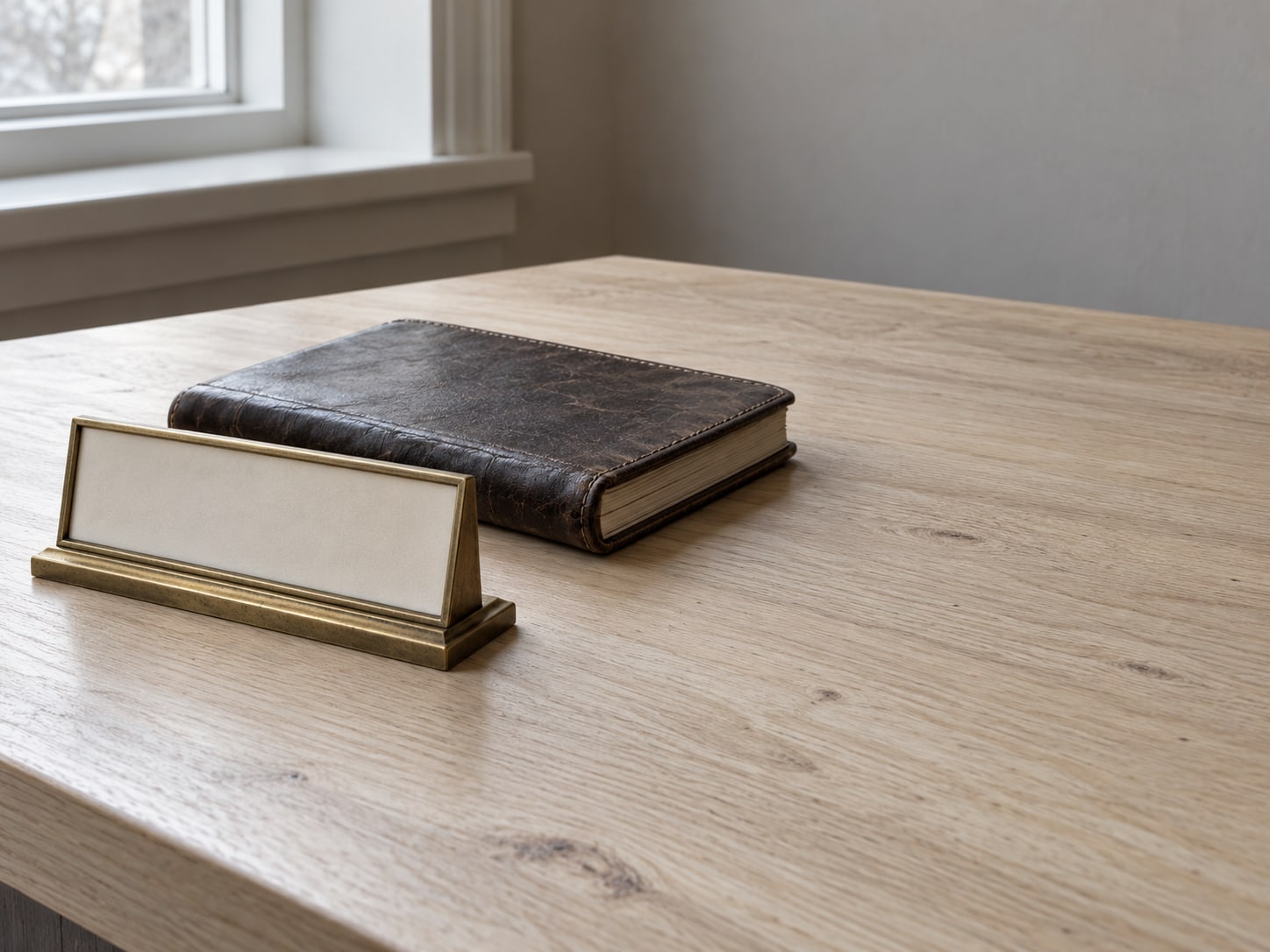 Un soporte de placa de latón y una agenda de citas de piel cerrada sobre un escritorio de recepción de madera, limpio.